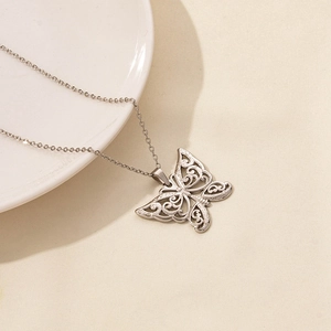 Close-up of a silver hollow butterfly pendant necklace on a textured beige background