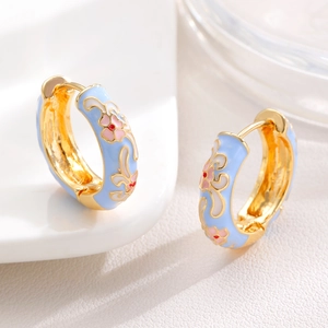 Macro shot of light blue enamel hoop earrings with pink flower patterns and gold trim