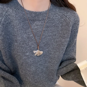 Detailed view of silver ginkgo leaf pendant on a dark brown cord necklace for women