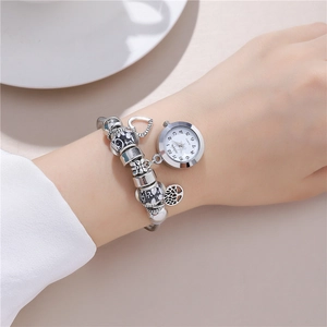 Silver beaded bracelet watch with heart and tree charms on a woman's wrist