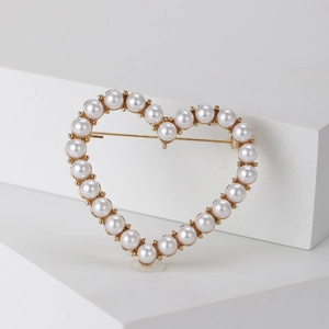 Detail shot of heart-shaped brooch with white faux pearls on elegant gold alloy metal base