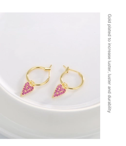 Detail of gold plated heart earrings with purple zircon inlay and polished finish