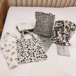 Detail view of four minimalist black and white floral canvas tote bags on a bed