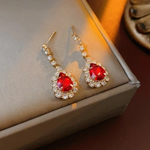Close-up of golden red teardrop gemstone earrings with glittering diamond borders