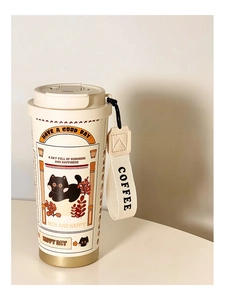 Detail of the cream coffee tumbler featuring a cute black cat illustration and a carry strap