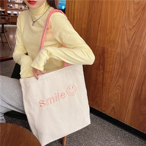 Detail of embroidered pink smile text on beige canvas tote bag with woven shoulder strap