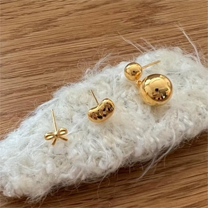 Close-up of 925 sterling silver gold stud earrings in bow and bean designs on soft fabric