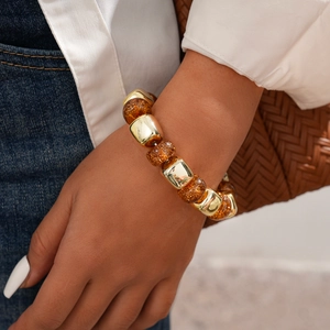 Close-up of golden metal beads and amber resin bracelet worn by a model in casual attire