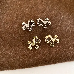 Hollow horse stud earrings in gold and silver colors on a textured plush background