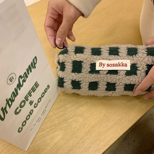 Close-up of hand opening a green waffle fleece pencil case with checkerboard pattern