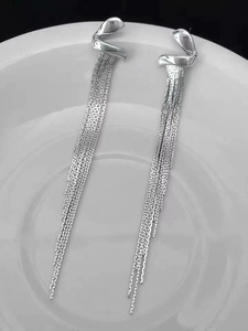 Macro shot of silver geometric tassel earrings with fine metal chains on white ceramic