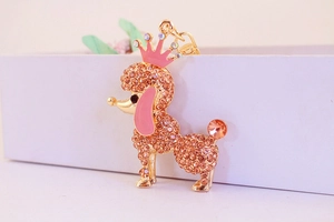 Detail of a golden poodle keychain with pink rhinestones and a crown on a white box