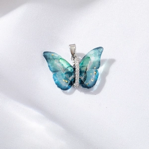 Blue-green gradient butterfly pendant with gold sequins and diamond inlay on white fabric