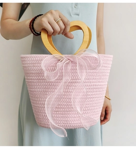 Close-up of pink woven handbag with wooden heart handle and delicate tulle bow detail