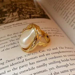 Bague ouverte à perle ovale irrégulière dorée sur des pages de livre vintage