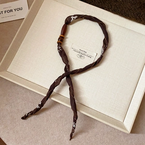 Detail of dark brown fabric necklace with floral pattern and vintage wood bead on tray