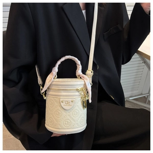 Detail of cream barrel bag with debossed patterns and pink silk scarf on handle