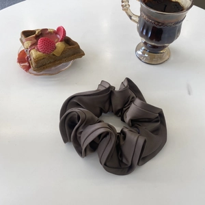 Elegant dark brown satin scrunchie with pleated texture on white table with breakfast