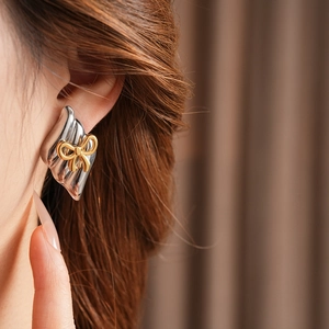 Close-up of diamond-shaped silver earrings with gold bow detail worn by a model