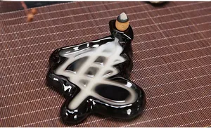 Close-up of black ceramic backflow incense burner with Shou character design and smoke