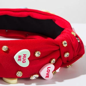 Detailed close-up of red knotted headband with rhinestone accents and heart resin charms