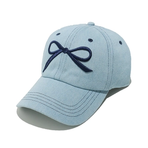 Detail of light blue denim baseball cap with navy bow embroidery and reinforced stitching