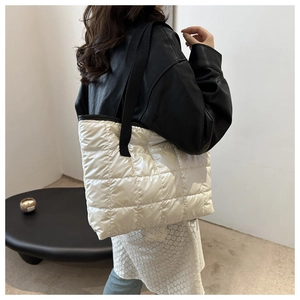 Detail of white quilted puffer tote bag with black wide strap shown on shoulder