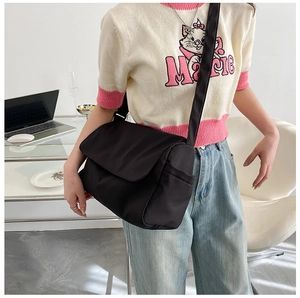 Close-up of black oversized nylon crossbody bag with flap closure and adjustable strap