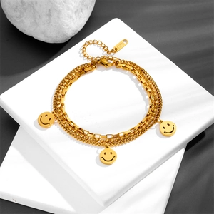 Layered gold smiley face charm bracelet made of stainless steel on white stone display