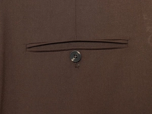 Detail of the brown trousers showing a sewn welt pocket and dark four-hole button