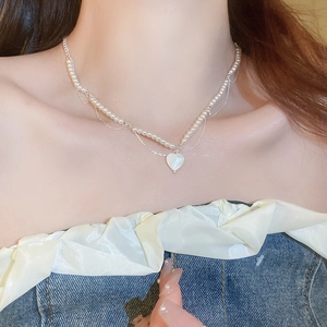 Gros plan du collier de perles avec pendentif cœur blanc sur cou et clavicule élégants
