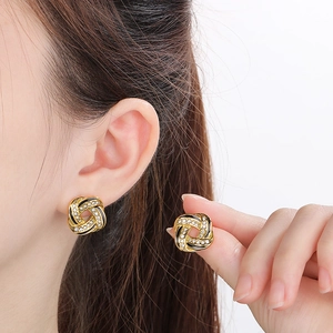 Detailed close-up of golden woven knot earrings with black enamel and sparkling zircons