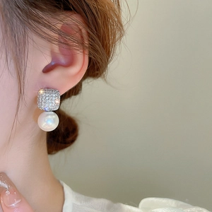 Detailed view of luxury square zircon and white pearl drop earrings on a model's ear