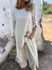 Detail of loose beige linen two-piece set featuring irregular hem and metal button accents