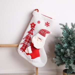 Close-up of white knitted Christmas stocking featuring Santa Claus and red plaid tree