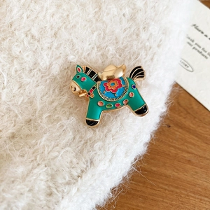 Close-up of green enamel horse brooch with floral saddle on white plush background