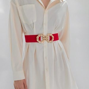 Detail of red elastic waist belt with twisted gold metal buckle on white shirt dress