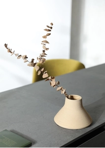 Close-up of beige brushed ceramic vase with horizontal texture and dried eucalyptus leaf