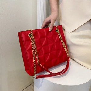 Detailed view of red quilted shoulder bag with gold chain strap and geometric texture