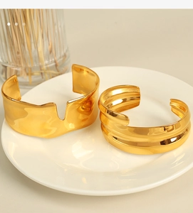 Detail view of two gold-plated titanium steel cuffs with irregular wavy and layered designs