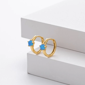 Detail of gold hoop earrings with blue opal stones on minimalist white geometric stands