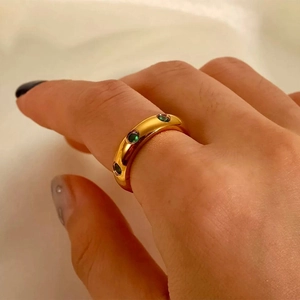 Gros plan d'une bague dorée 18 carats avec trois pierres vertes sur la main