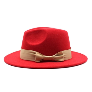 Close-up of red wide-brimmed felt fedora hat featuring a champagne ribbon and bow detail