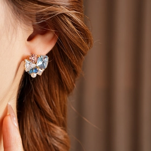 Close-up of geometric gold earrings with pink and blue stones and a pearl inlay