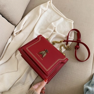 Red crossbody bag with vintage bee buckle and gold chain strap on beige sofa
