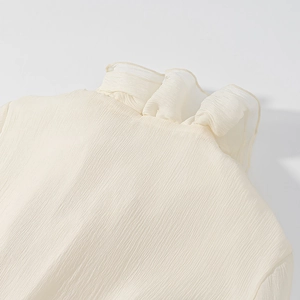 Detailed close-up of ruffle collar and pleated texture on cream white blouse
