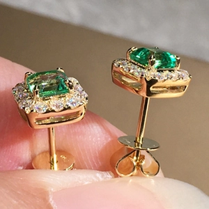Macro shot of 18K gold emerald-cut green stone earrings with a halo of white zircon