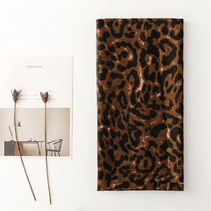 Flat lay of leopard print cotton linen scarf with dry flowers and magazine on white desk