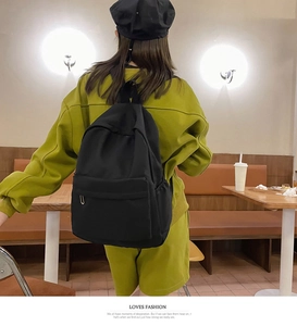 Lifestyle shot of a black minimalist canvas backpack worn by a model in a cafe