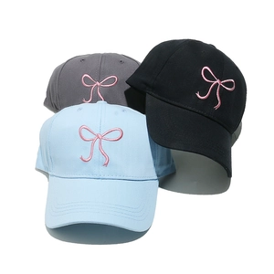 Detailed stack of cotton baseball caps in black, grey, and blue with pink bow embroidery